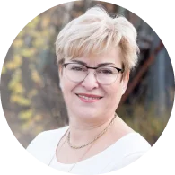 Porträtfoto einer lächelnden Frau mit kurzen blonden Haaren und Brille in weißer Bluse