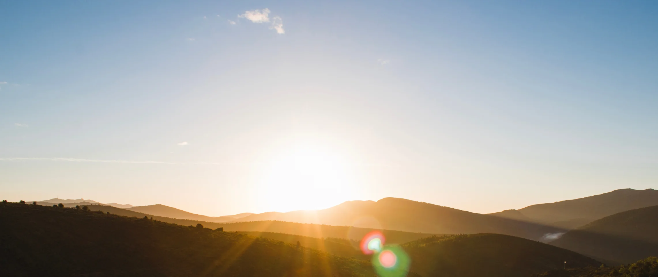 Sonnenaufgang über Hügellandschaft mit warmem Lichtschein und Lens-Flare-Effekt