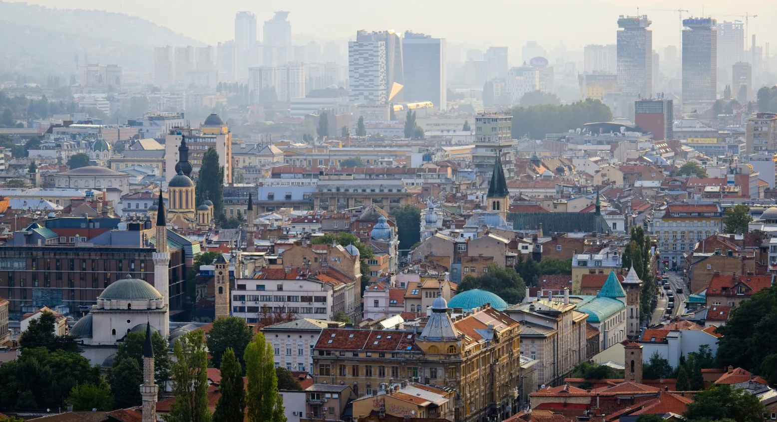 Stadtpanorama mit Moscheeminaretten, historischen Kirchtürmen und modernen Hochhäusern im Dunst