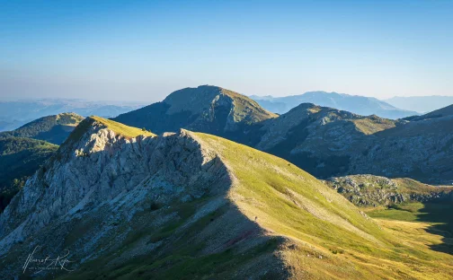 Grüner Bergrücken mit Felsgipfeln und Wanderweg im Abendlicht