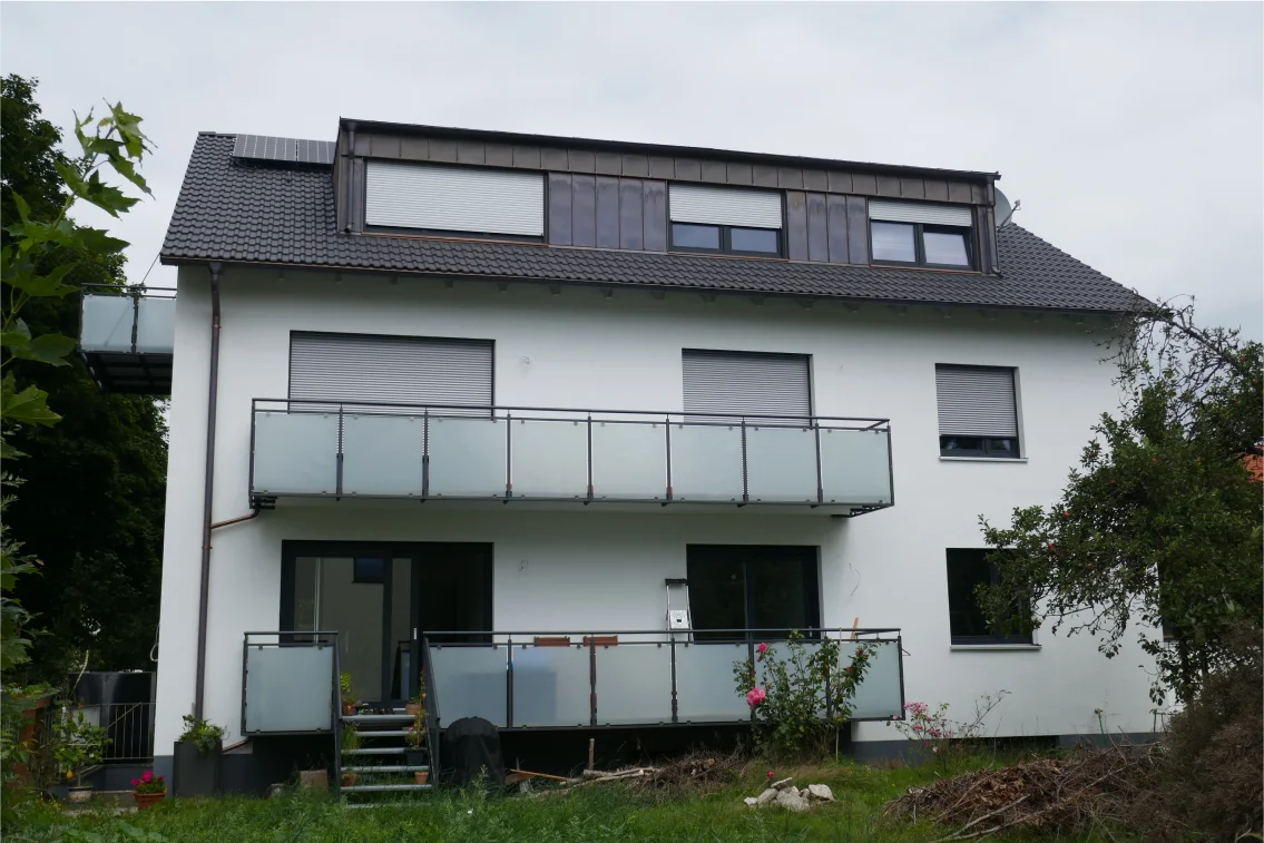 Weißes Mehrfamilienhaus mit zwei Balkonebenen und Glasgeländer vor grünem Garten