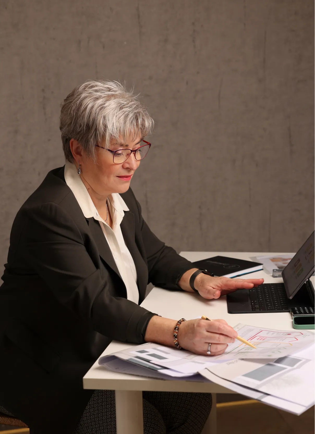 Person am Schreibtisch mit Tablet, Notizbuch und Plänen bei der Büroarbeit
