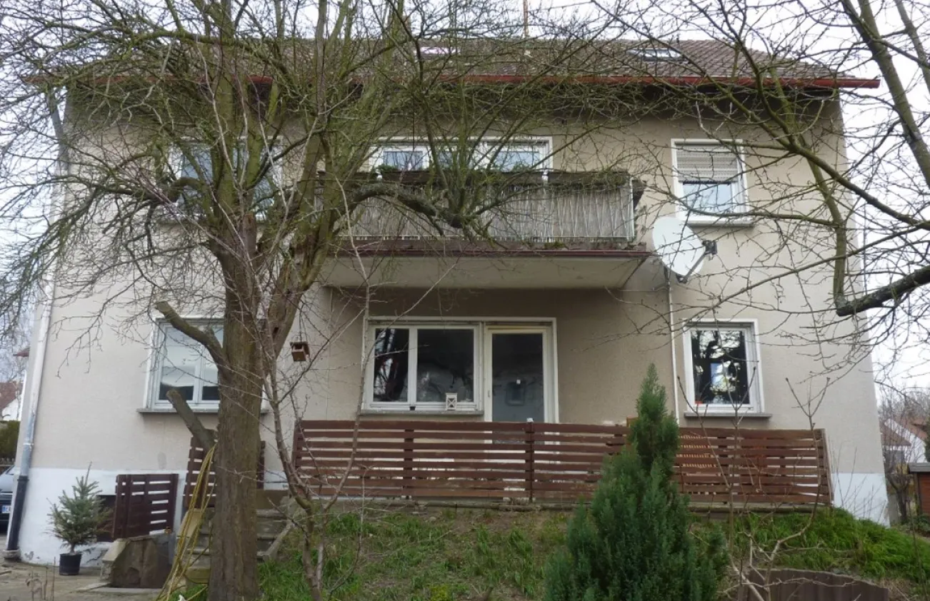 Beiges zweistöckiges Haus mit Balkon und Holzzaun hinter kahlen Bäumen
