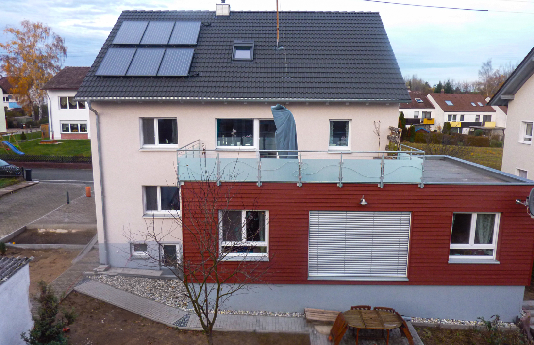 Zweistöckiges Haus mit weißer Fassade, rotem Anbau und Solarkollektoren auf dem Dach