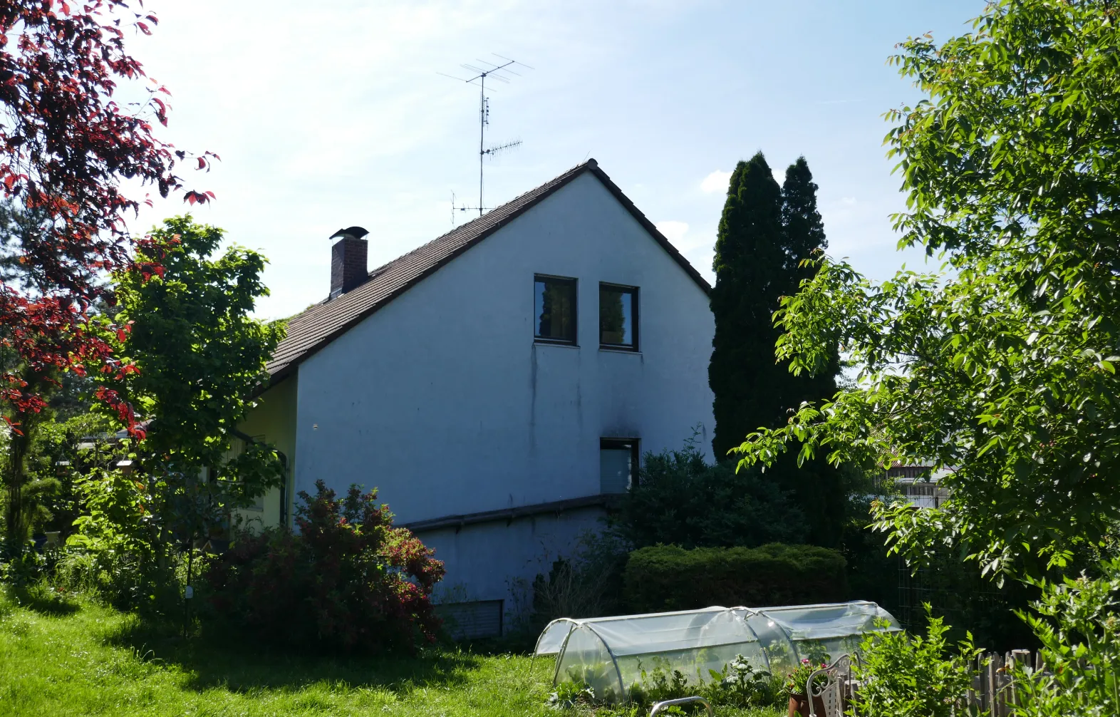 Weißes Haus mit Ziegeldach und Garten, im Vordergrund ein Folientunnel für Pflanzen