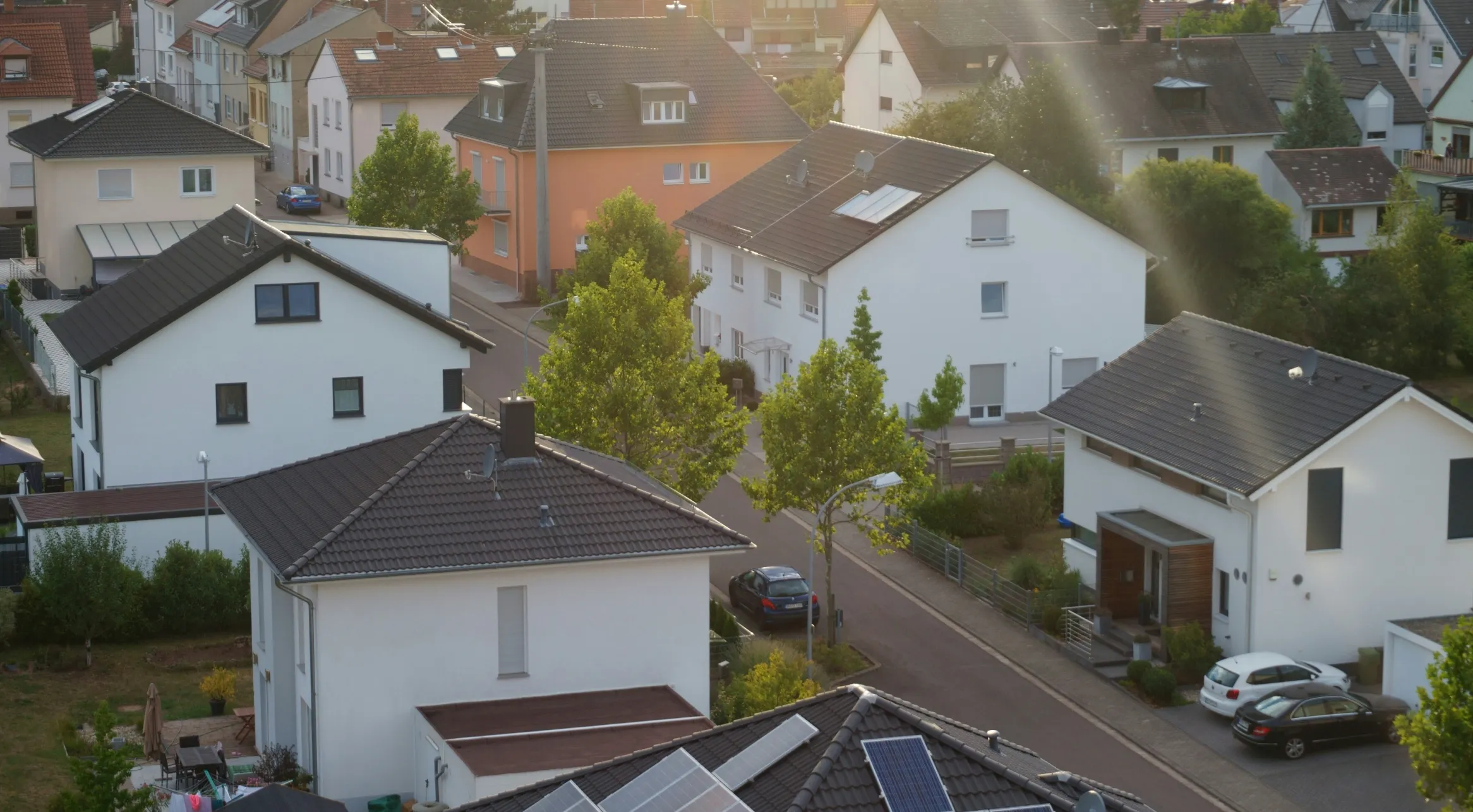 Luftaufnahme einer Wohnsiedlung mit weißen Häusern, Ziegeldächern und einer Straße im goldenen Abendlicht