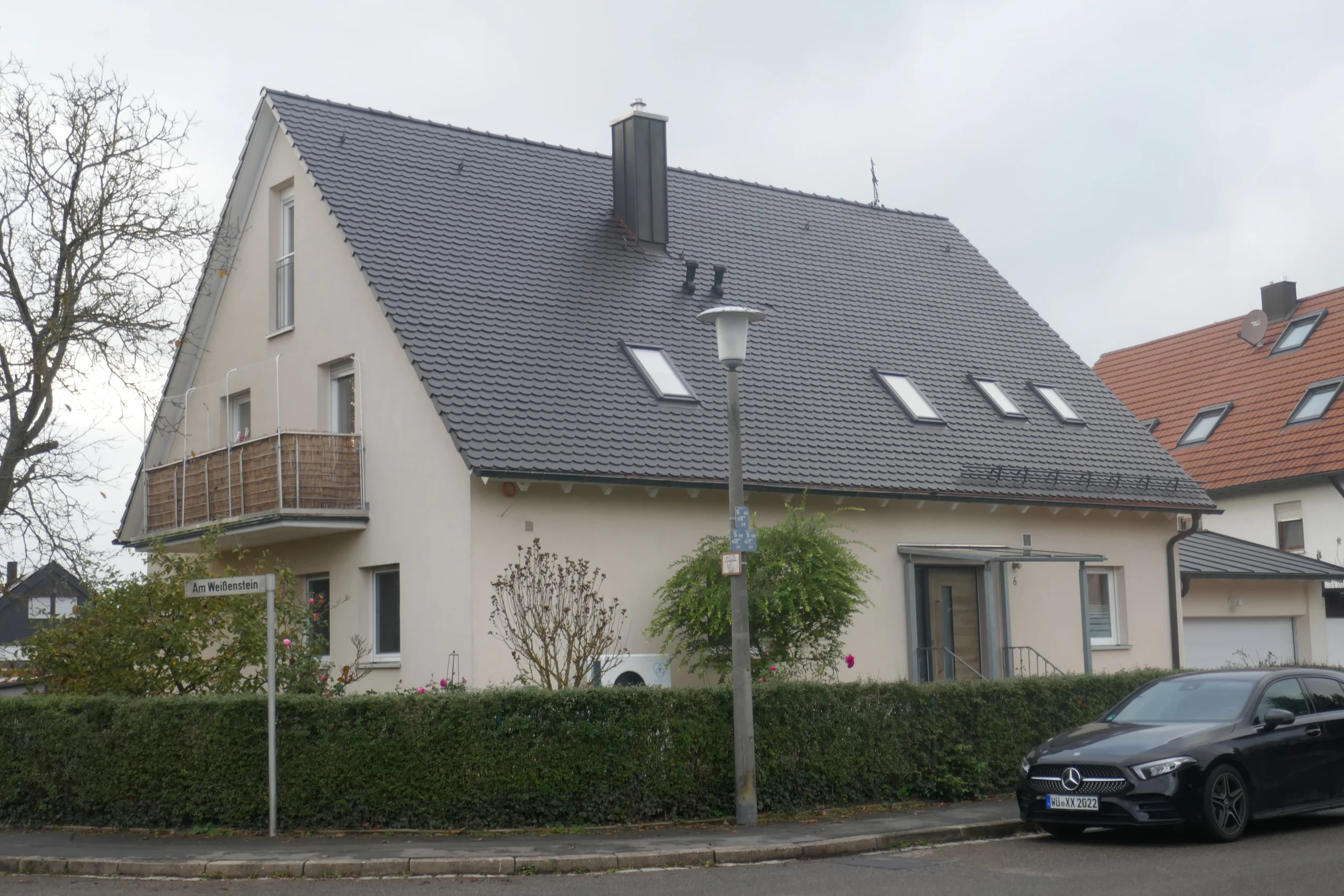 Zweistöckiges Einfamilienhaus mit Satteldach, Dachfenstern und Balkon hinter einer Hecke