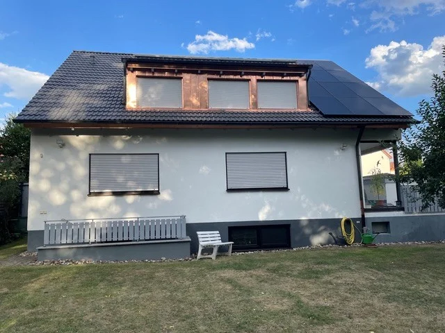 Weißes Einfamilienhaus mit Solaranlage auf dem Dach, Fenstern mit Rollläden und gepflegtem Garten