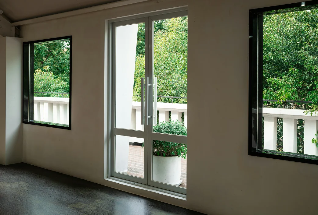 Leerer Raum mit weißer Balkontür und zwei Fenstern mit Blick auf grüne Bäume