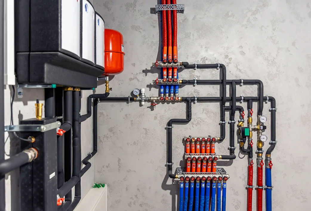 Technikraum mit Heizungsanlage, rotem Ausdehnungsgefäß und Verteilern für rote und blaue Heizungsrohre