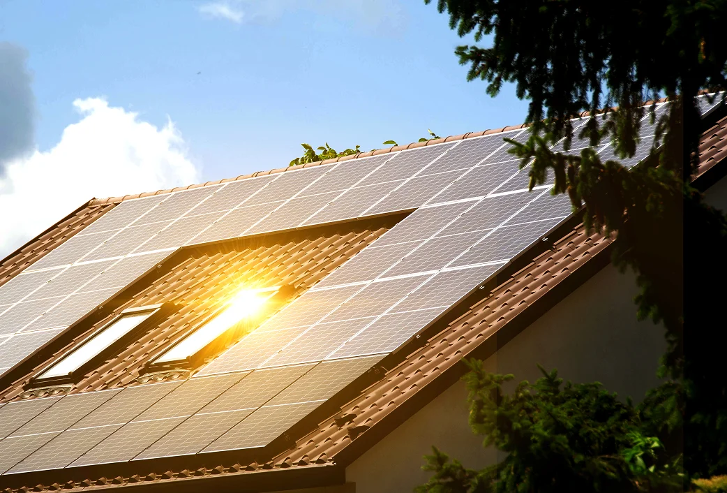 Solarpanels auf rotem Ziegeldach mit Sonnenreflexion in zwei Dachfenstern